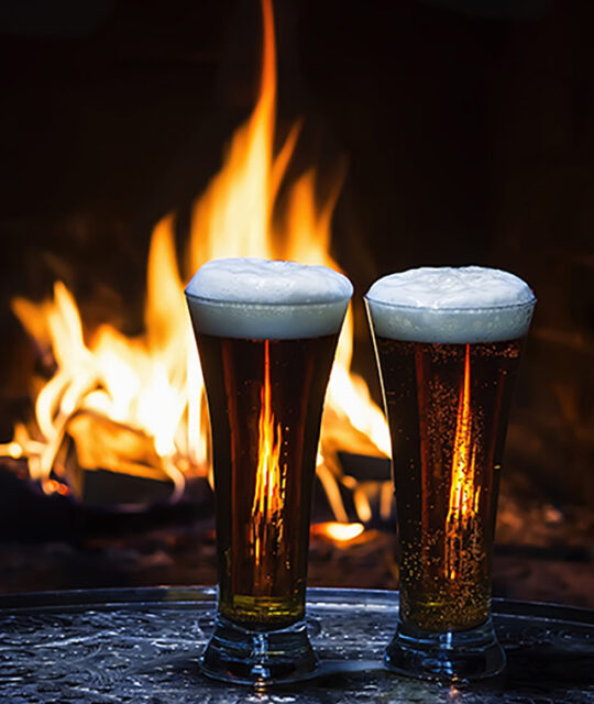 Two pilsners in front of a fireplace