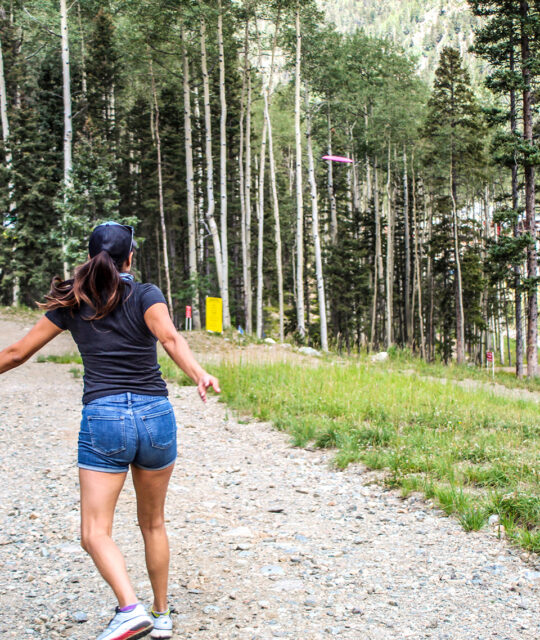 A woman playing disc golf on a mountain course in aspen trees