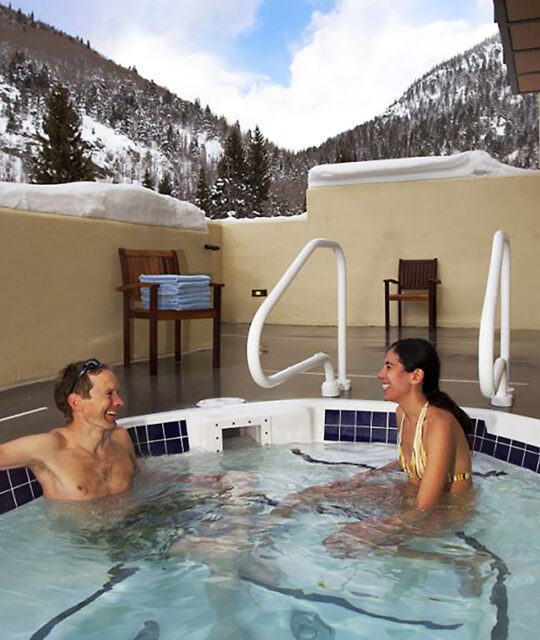 Couple enjoying an après ski soak in the outdoor hot tub with snowy forest behind.