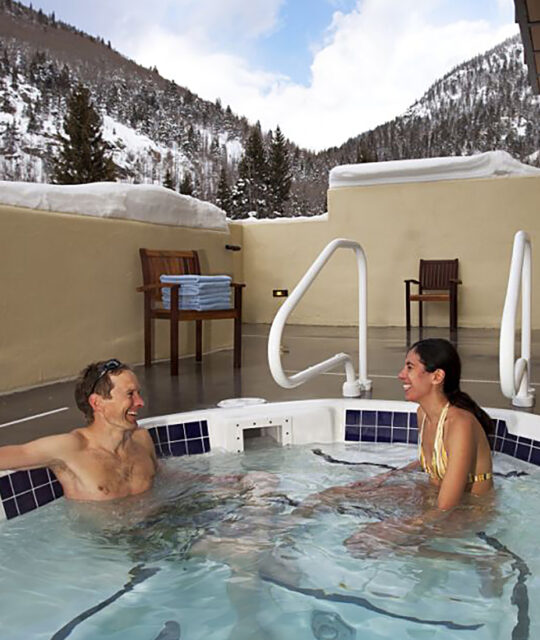Couple enjoying an après ski soak in the outdoor hot tub with snowy forest behind.