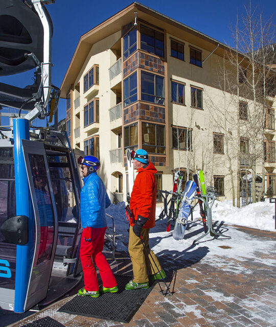 Skiers entering gondola from hotel terrace.