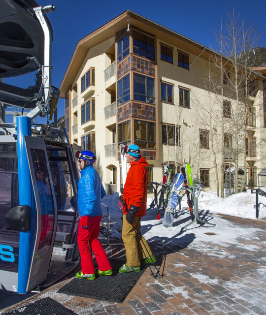 Skiers entering gondola from hotel terrace.