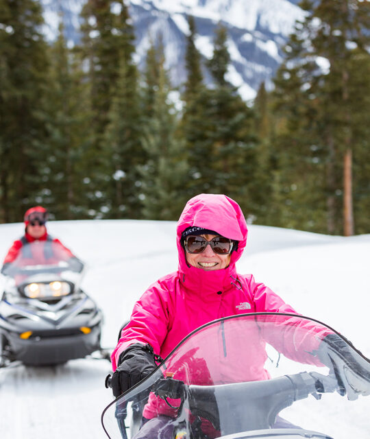 A woman in a bright pink jacket riding a snowmobile