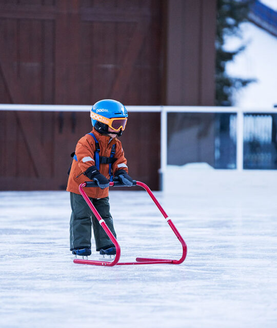 Child ice skating using a skate pusher trainer.