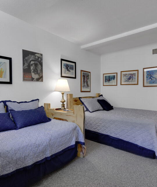 Twin beds in condo bedroom with framed photos of skiers at Taos Ski Valley on walls.