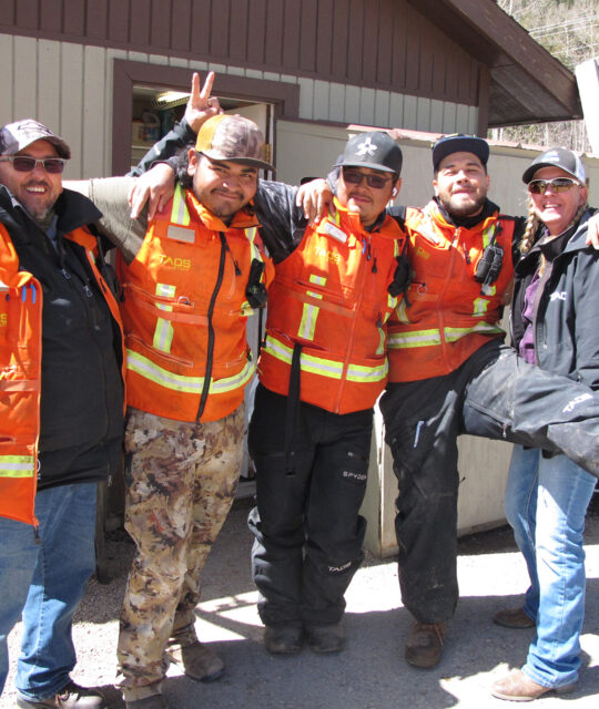 Men in orange safety vests smile arm in arm.
