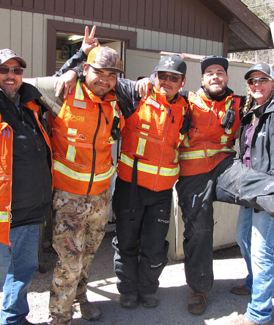 Men in orange safety vests smile and joking around.