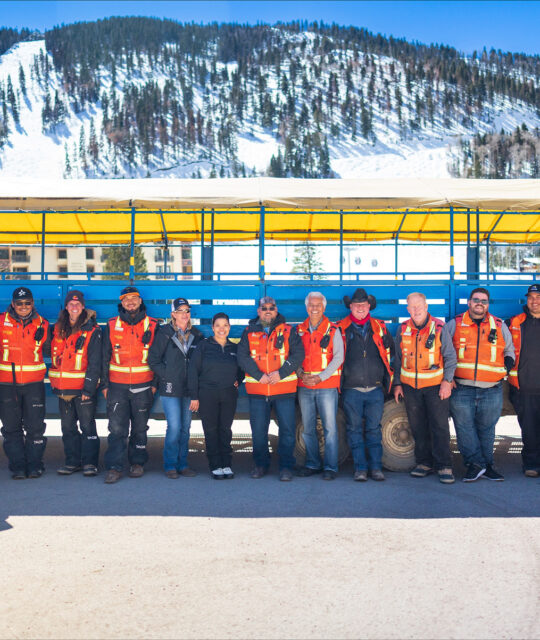 A group of people in orange safety vests pose in front of a blue shuttle car.