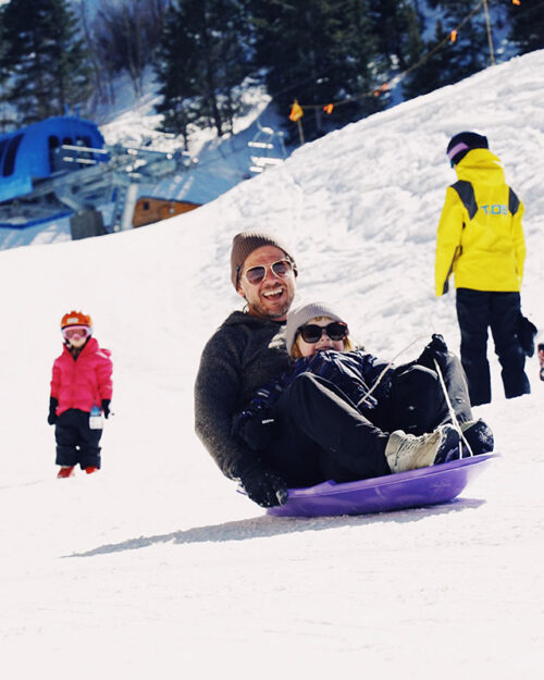 A father and child ride a sled together at Taos sledding hill.