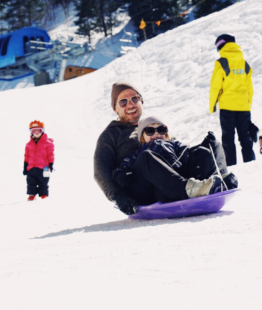 A father and child ride a sled together