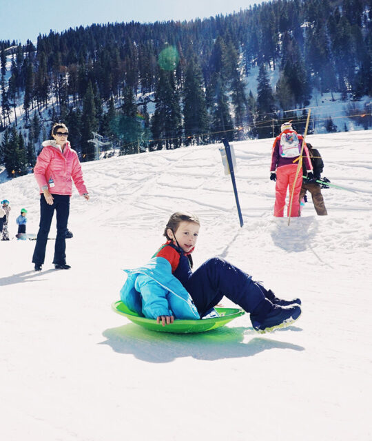 Girl slides down a hill on a green sled.