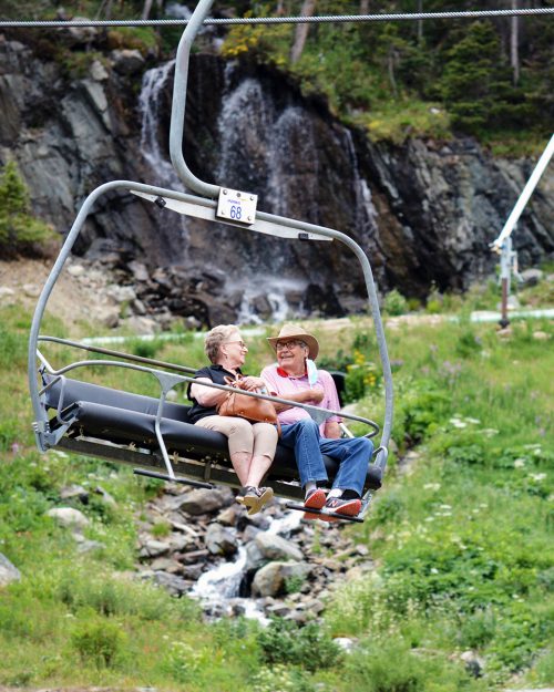 Older couple enjoying a scenic summer chairlift ride with a waterfall in the background