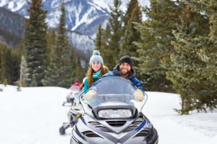 Couple snowmobiling together winding up a snowy hill with friends behind.