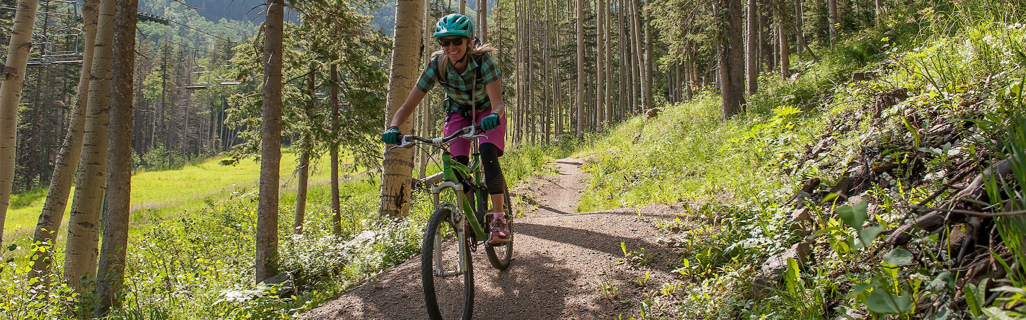 A woman rides a mountain bike down a trail through a grove of aspens