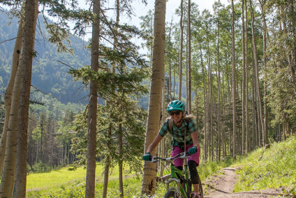 A woman rides a mountain bike down a trail through a grove of aspens in summer