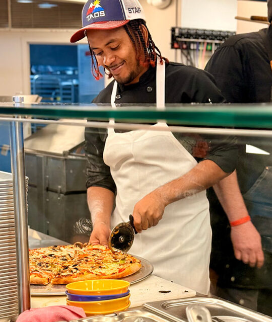 Taos employee slicing a fresh pizza.