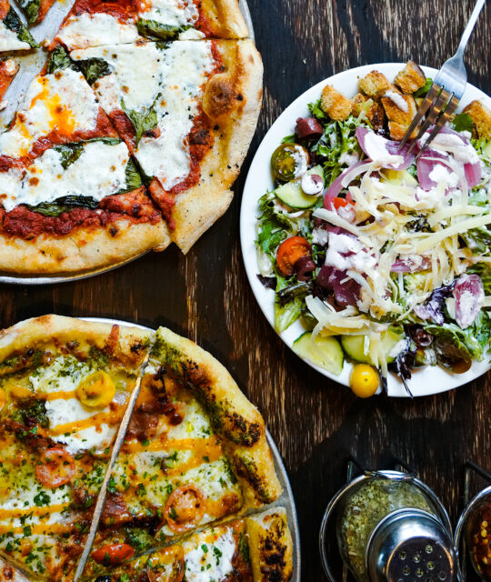 Overhead shot of pizzas and salad