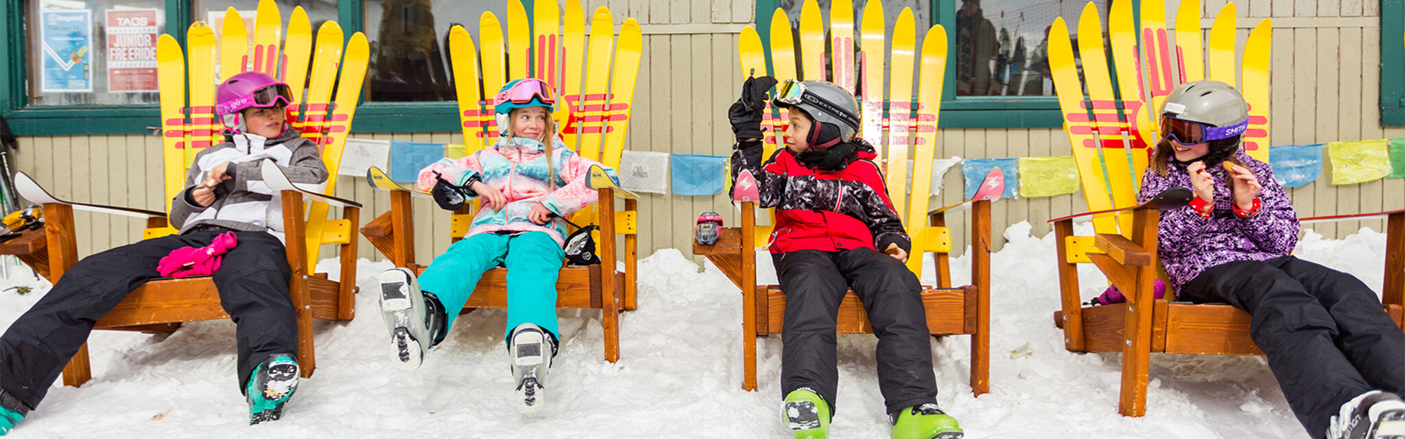 Kids make faces while taking a ski break in brightly colored Adirondak chairs