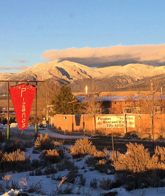 Pizaños pizza and pasta sign and winter sunset on Taos mountains.