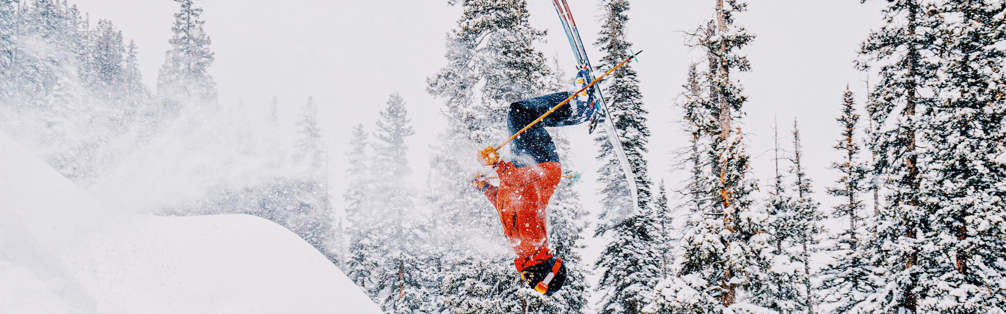 A skier flips upside down off a powdery ledge