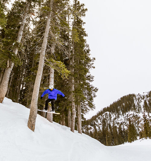 A snowboarder catches air coming out of the trees at Taos Ski Valley