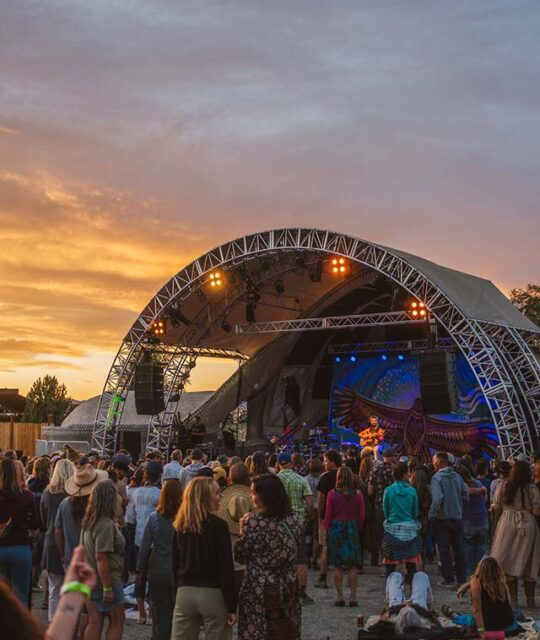 Outdoor concert venue at sunset, with a packed crowd.