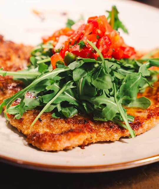 Thin pork cutlet with arugula and tomatoes.