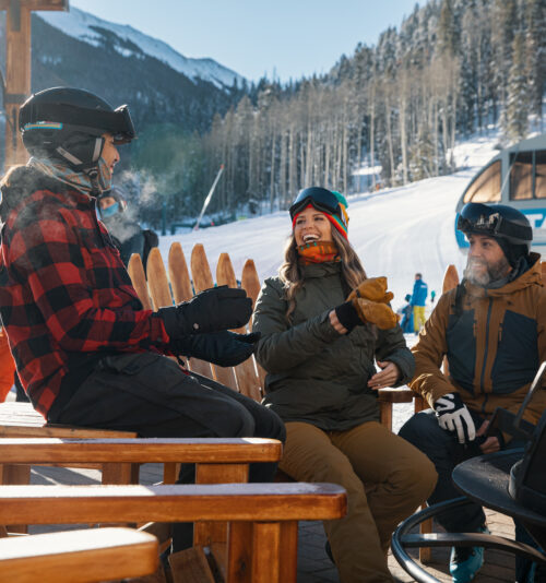 Friends laugh around a firepit in the snow at Taos Ski Valley