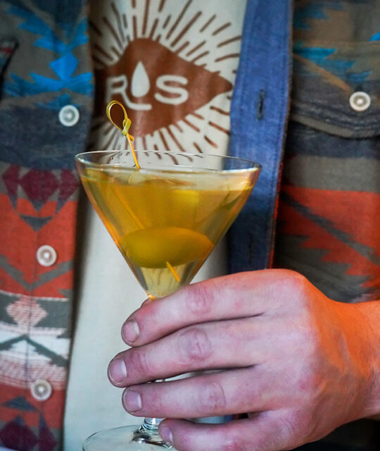 Man holding a martini wearing a Rolling Still shirt