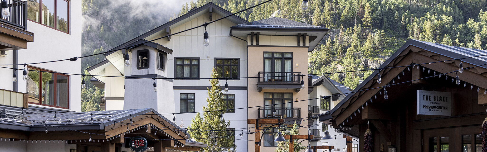 A stately condo-hotel sits in front of treed mountains with hanging clouds.