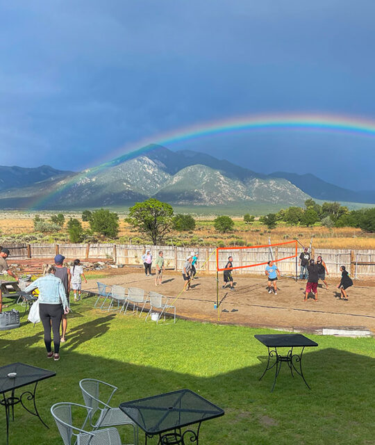 Volleyball players and rainbow and Taos Mountain as seen from the backyard of the KTAOS Solar Center.