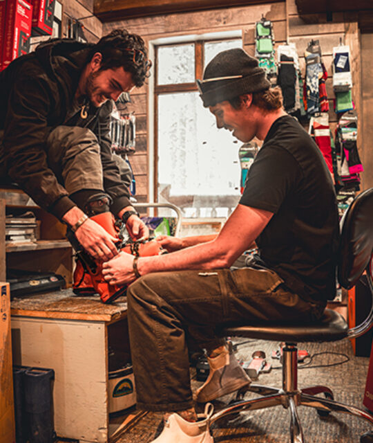 A man sits on platform to have ski boots fitted.