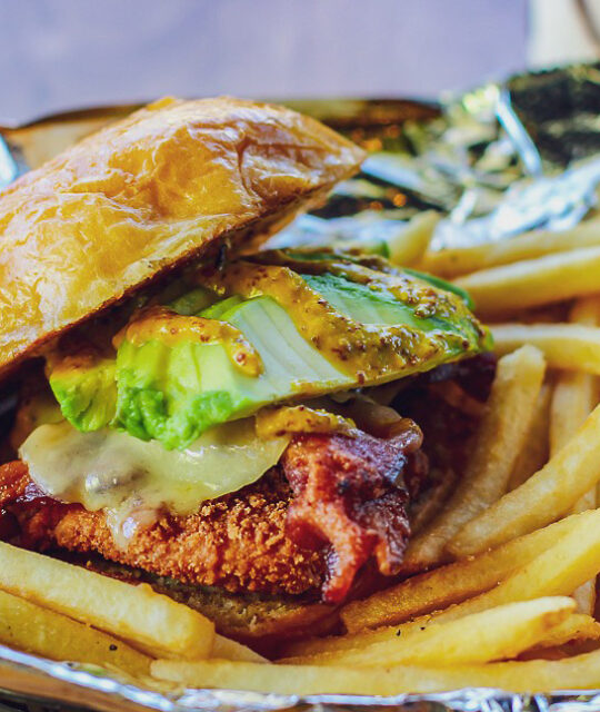 Fried chicken sandwich with avocado and fries.