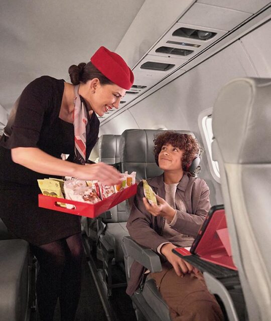 A flight attendant for JSX serving a in flight snack to a teen boy.