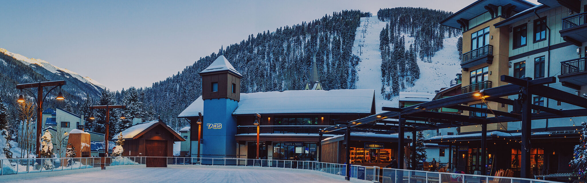 The low light of a frosty evening falls over an empty ice rink and ski slopes.