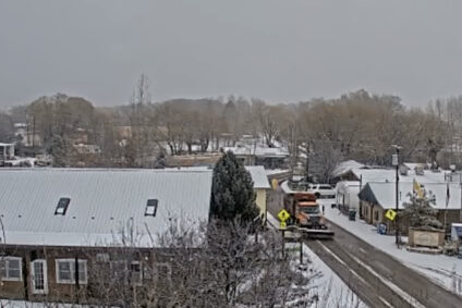 A snowplow drives down a cleared road in a snowy viallage.