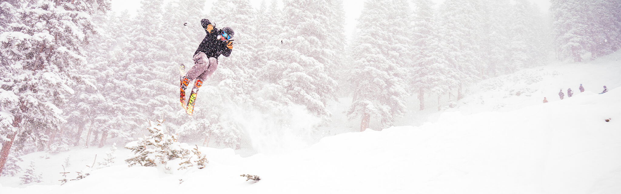 A lone skier flies sideways through the air on a snowy day.