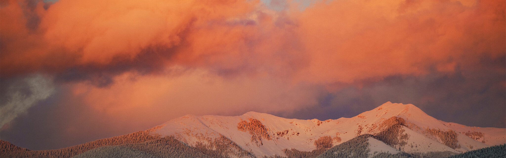 Alpenglow sets in across snow covered mountains and a large embankment of clouds.