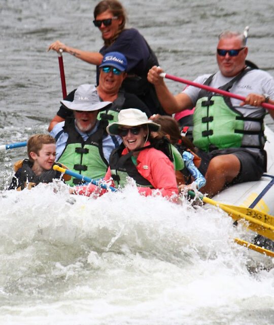 Whtewater rafting guide and customers on river.