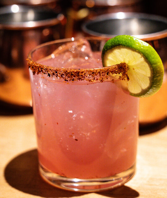 A pink cocktail with a chili rim and lime garnish.