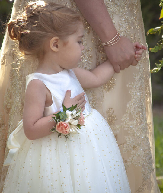 Adorable flower girl holding the hand of her mother.