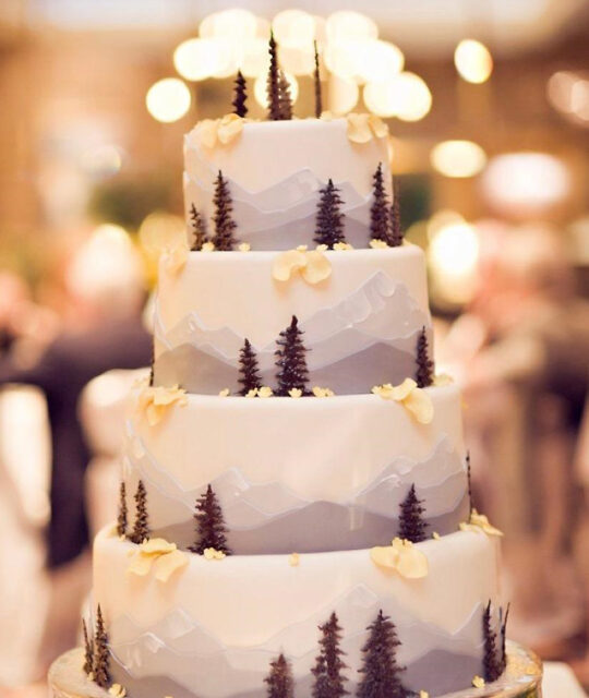 Wedding cake decorated with mountains and pine trees at the reception.