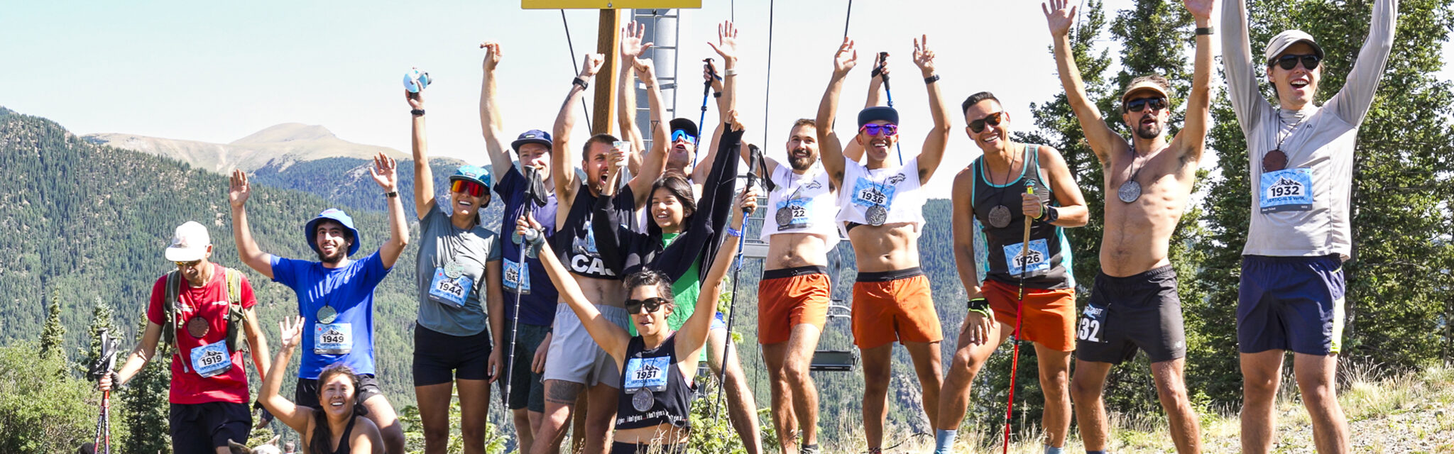 A group of runners stand at the finish line on top of a mountain with their arms raised in the air.