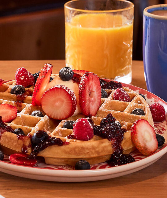 Breakfast waffle topped with fruit and glass of orange juice and coffee.