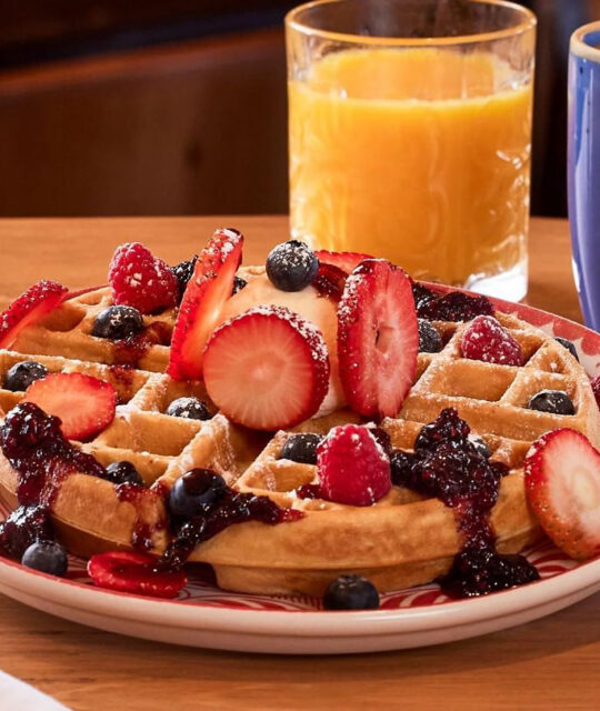 Waffles with berries and glass of orange juice.