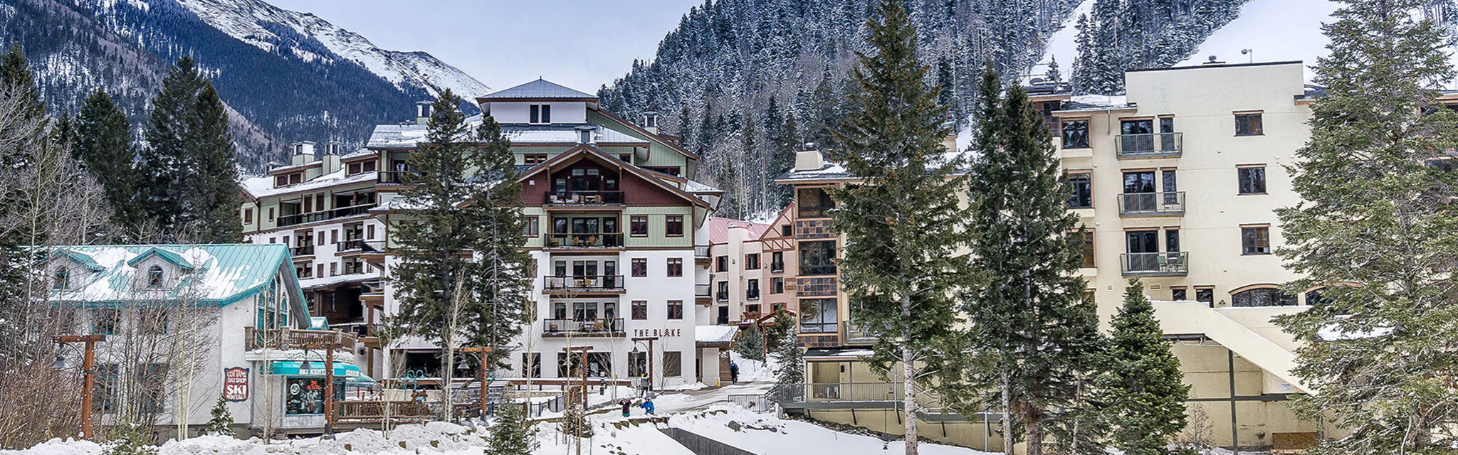 A snowy village of alpine condo buildings sit at the base of a ski slope.