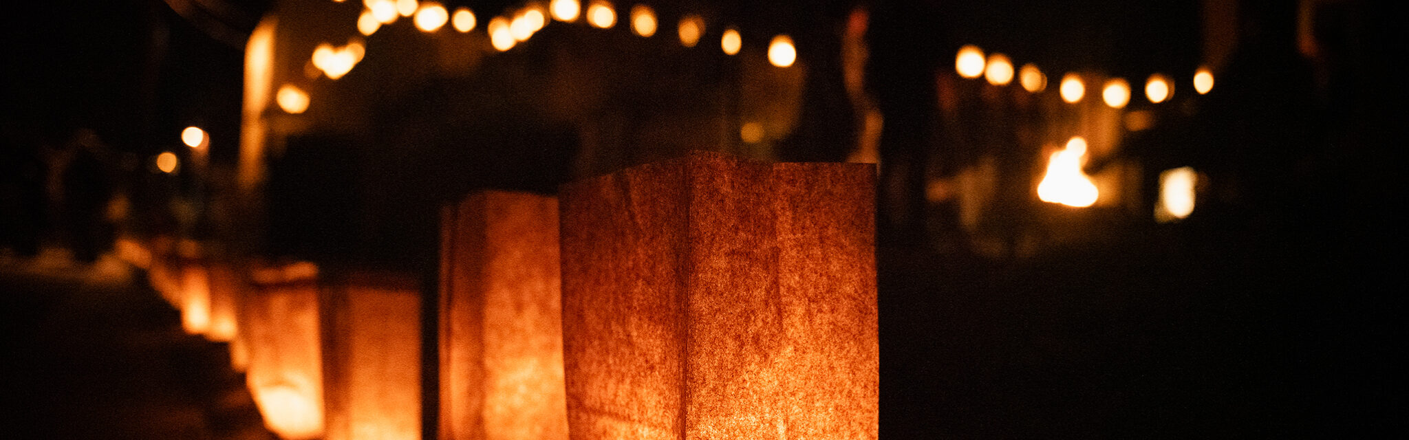 Farolitas light a darkened street and outline the top of a building.