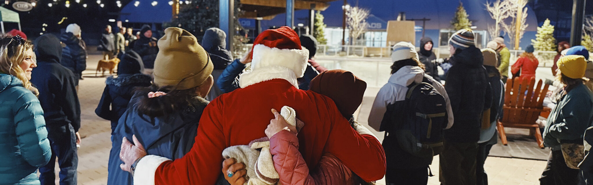 Santa and friends stand with their arms around each other facing away from the camera.