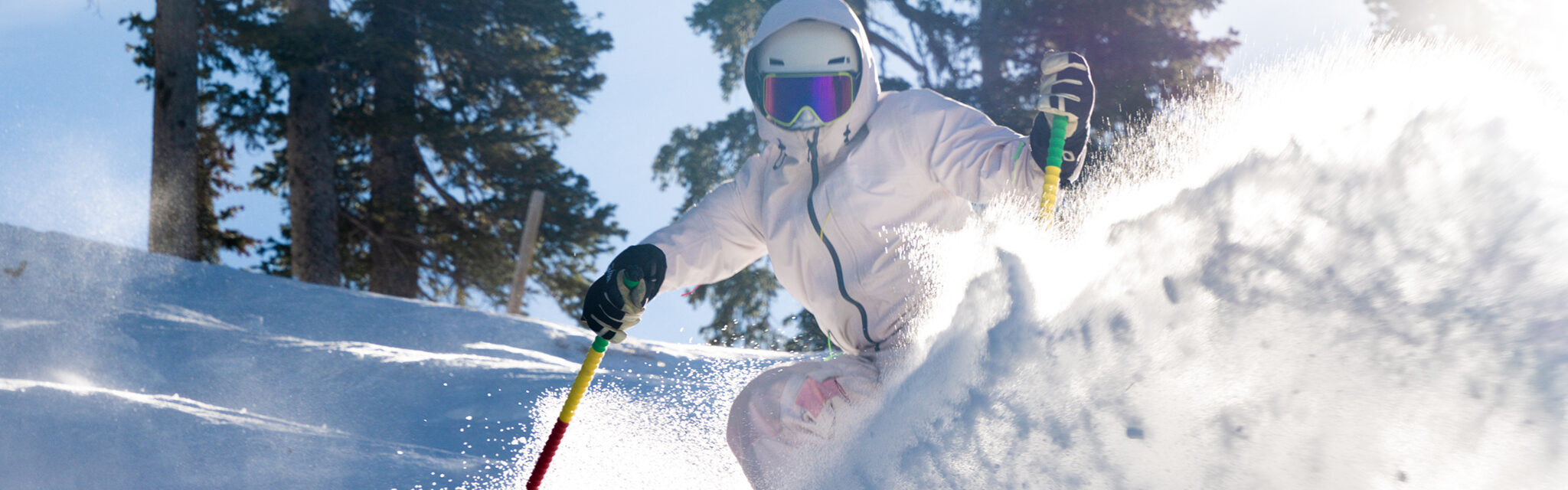 A skier clad all in white shoots powder up on a turn.