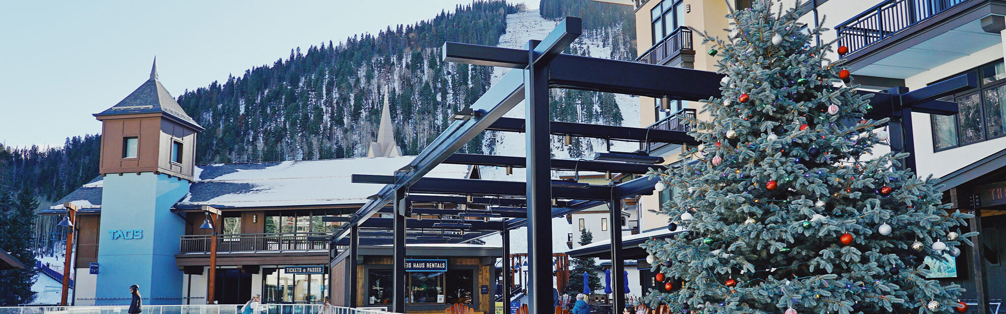 A few people skate on an outdoor ice rink next to a decked out Christmas tree.